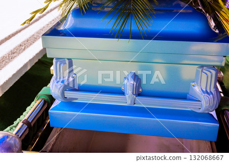 Blue casket surrounded by greenery is placed in cemetery for burial ceremony on funeral day. 132068667