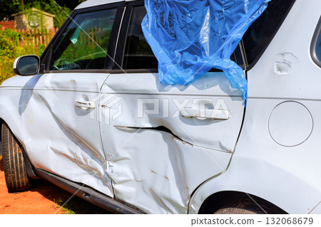 It is parked white car shows visible damage on side, with blue plastic covering part of dent 132068679