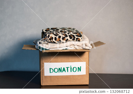 Woman folding clothes and placing them into donation box. Concept of charity and wardrobe decluttering. 132068712