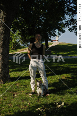 Woman standing with her red merle Border Collie puppy sitting at her feet on grass, trees and monument in background, Kalemegdan Woman standing with her red merle Border Collie puppy sitting at her feet on grass, trees and monument in background, Kalemegdan 132068753