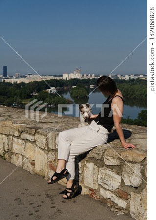 Woman sits with red merle Border Collie puppy on fortress wall at Kalemegdan, overlooking Belgrade city and river. Travel with dog concept Woman sits with red merle Border Collie puppy on fortress wall at Kalemegdan, overlooking Belgrade city and river. Travel with dog concept 132068828
