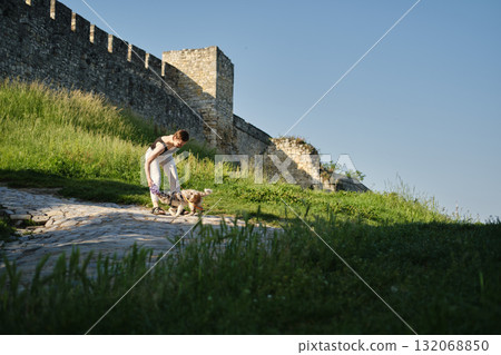 Young woman plays with red merle Border Collie puppy near Kalemegdan historic stone fortress wall under clear blue sky. Travel with dog concept Young woman plays with red merle Border Collie puppy near Kalemegdan historic stone fortress wall under clear blue sky. Travel with dog concept 132068850