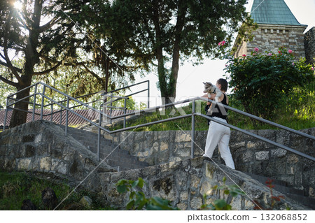 Woman carries red merle Border Collie puppy up stone stairs in park, walking together in warm sunlight 132068852