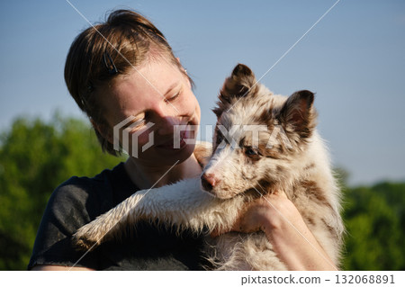 Woman lovingly looks at red merle Border Collie puppy in her arms, sharing an affectionate outdoor moment together 132068891