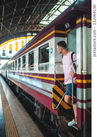 traveler guy boarding train at busy railroad station, young man with backpack starting journey on railway platform traveler guy boarding train at busy railroad station, young man with backpack starting journey on railway platform 132069190