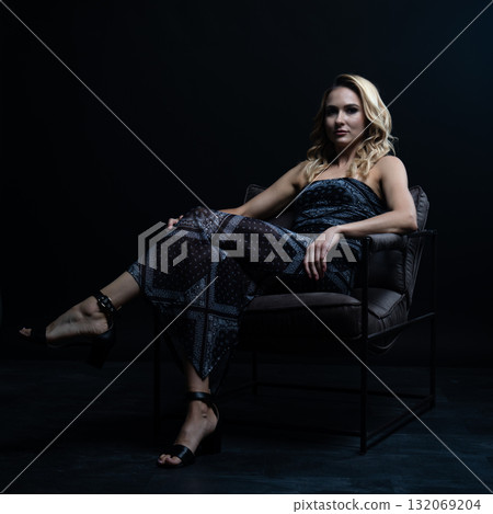 Blond fashion model posing on wooden chair in studio with dark background 132069204
