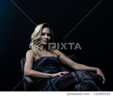 Blond fashion model posing on wooden chair in studio with dark background Blond fashion model posing on wooden chair in studio with dark background 132069205