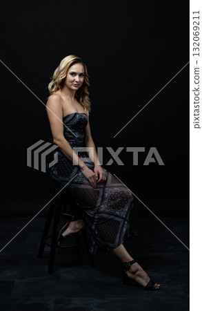 Blond fashion model posing on wooden chair in studio with dark background Blond fashion model posing on wooden chair in studio with dark background 132069211