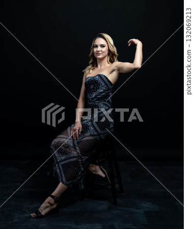 Blond fashion model posing on wooden chair in studio with dark background 132069213