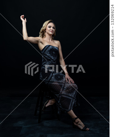 Blond fashion model posing on wooden chair in studio with dark background 132069214