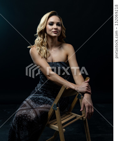 Blond fashion model posing on wooden chair in studio with dark background Blond fashion model posing on wooden chair in studio with dark background 132069218