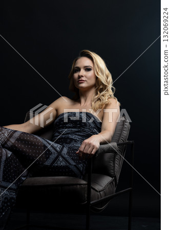 Blond fashion model posing on wooden chair in studio with dark background 132069224