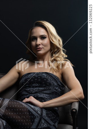 Blond fashion model posing on wooden chair in studio with dark background 132069225