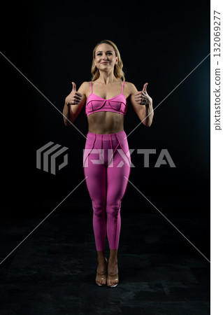 Confident fitness model posing in pink sportswear on black background Confident fitness model posing in pink sportswear on black background 132069277