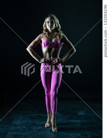 Confident fitness model posing in pink sportswear on black background Confident fitness model posing in pink sportswear on black background 132069296