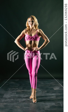 Confident fitness model posing in pink sportswear on black background 132069298