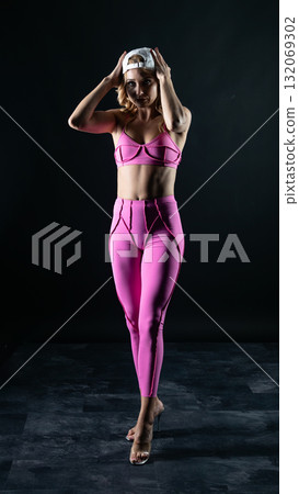 Confident fitness model posing in pink sportswear on black background 132069302