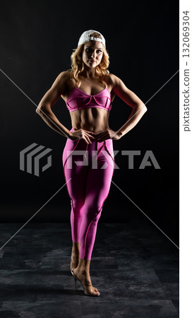 Confident fitness model posing in pink sportswear on black background 132069304
