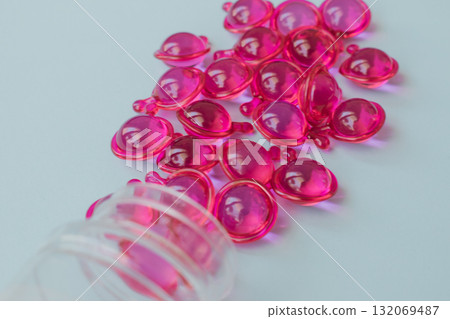 Vibrant pink hair serum capsules spilling from a plastic bottle, for dry, damaged and frizzy hair. Close-up light blue background Vibrant pink hair serum capsules spilling from a plastic bottle, for dry, damaged and frizzy hair. Close-up light blue background 132069487
