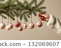 Christmas ornaments hang on a pine branch and a hand touches one of them. 132069607