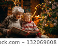 Grandmother and child reading a book near Christmas tree lights. 132069608