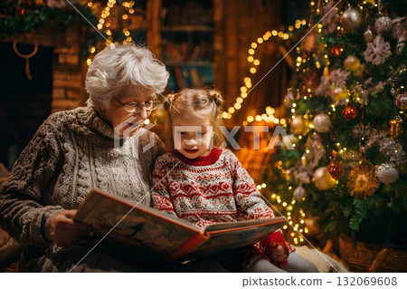 Grandmother and child reading a book near Christmas tree lights. 132069608