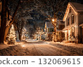 A snowy street lined with houses decorated for Christmas lights glows warmly at night. 132069615