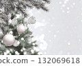 Christmas ornaments hang from a frosted pine branch with soft bokeh lights. 132069618