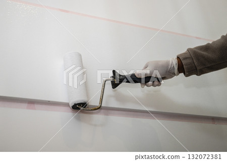 A close-up of a hand in a protective glove painting a light-colored wall with a roller A close-up of a hand in a protective glove painting a light-colored wall with a roller 132072381