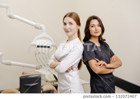 Smiling dentist and assistant with crossed hands looking at the camera in dental clinic 132072407