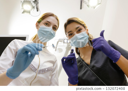 From below female dentists with mirror and device bending over patient during appointment in dental clinic 132072408