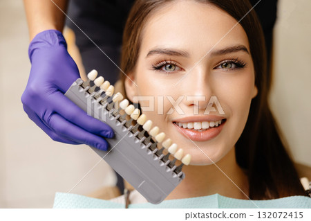 Dentist choosing teeth enamel shade color for young smiling female patient before whitening procedure 132072415