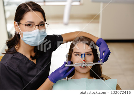 Female dentist trying on a facial arch for a patient sitting in a dental chair 132072416