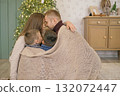 A family wraps themselves in a knitted warm cozy blanket sitting by the Christmas tree on a winter morning 132072447