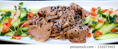 Serving of sliced boiled beef tongue with pickled cucumbers and bell peppers drizzled with olive oil soy sauce and crushed garlic topped with black and white sesame and microgreens on white plate. Serving of sliced boiled beef tongue with pickled cucumbers and bell peppers drizzled with olive oil soy sauce and crushed garlic topped with black and white sesame and microgreens on white plate. 132073403
