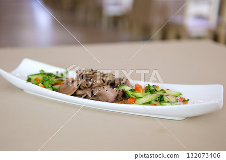 Serving of sliced boiled beef tongue with pickled cucumbers and bell peppers drizzled with olive oil soy sauce and crushed garlic topped with black and white sesame and microgreens on white plate. Serving of sliced boiled beef tongue with pickled cucumbers and bell peppers drizzled with olive oil soy sauce and crushed garlic topped with black and white sesame and microgreens on white plate. 132073406