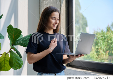 Young teenage girl using laptop for video chat conference standing at home 132073712