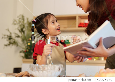 Joyful baking moments. Mother and daughter sharing festive cooking experience in cozy kitchen. 132073779