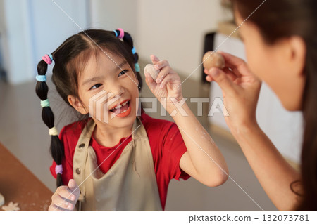 Creative Baking. Young girl and mother playfully shaping dough in a festive kitchen. 132073781