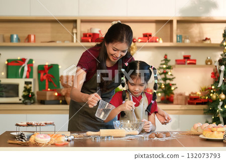 Baking Memories A mother and daughter mixing ingredients for holiday treats in a cozy kitchen 132073793