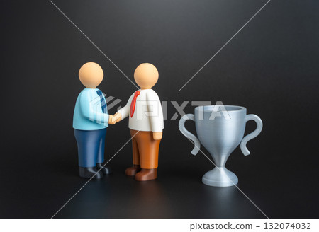 Two office workers shake hands near the winner's trophy. Recognition of success, award presentation, and teamwork. Leadership, career growth, and professional excellence. Two office workers shake hands near the winner's trophy. Recognition of success, award presentation, and teamwork. Leadership, career growth, and professional excellence. 132074032