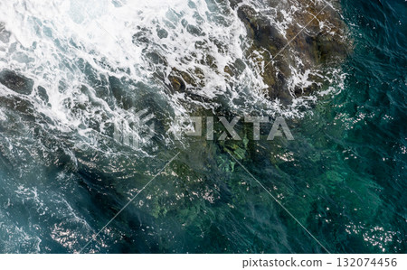 Aerial view of the turquoise sea meeting a rocky coast, natural photo background 132074456