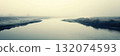 Serene misty wetland with tranquil water and dry grass in fog 132074593