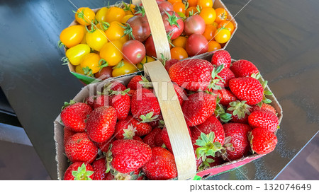 Fresh strawberries and cherry tomatoes in baskets on a dark wooden table, showcasing vibrant colors and natural textures for culinary inspiration 132074649