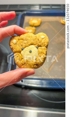 Cute bear-shaped cookie held by a hand, showcasing delightful baking creativity and fun dessert presentation in a kitchen environment 132074650