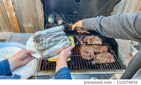 Grilling delicious steaks and wrapped vegetables on barbecue, showcasing vibrant outdoor cooking experience with friends and family gathering 132074656