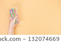 Hand holding a bag of colorful rubber bands against a bright solid orange background 132074669