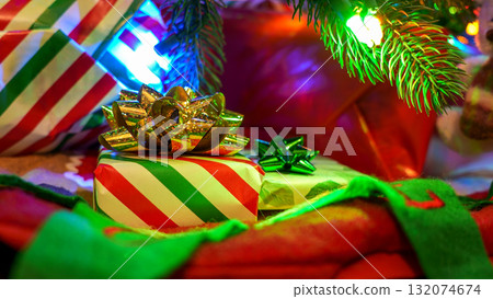 Striped Gift Box with Red Bow Under a Christmas Tree with Multicolored Lights 132074674