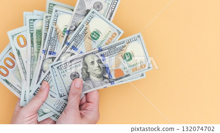 Stack of One Hundred Dollar Bills in Hand on Peach Color Background, Earning and Financial Freedom. Stack of One Hundred Dollar Bills in Hand on Peach Color Background, Earning and Financial Freedom. 132074702