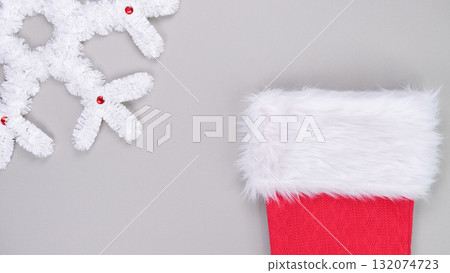Red Christmas stocking with fluffy white trim placed against a soft gray background, surrounded by decorative snowflakes for festive ambiance Red Christmas stocking with fluffy white trim placed against a soft gray background, surrounded by decorative snowflakes for festive ambiance 132074723